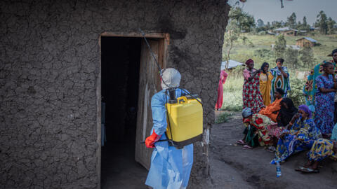Un bénévole, vêtu d'une combinaison de protection, désinfectant la porte d'une maison où se trouve un enfant, présumé décédé des suites de la maladie à virus Ebola, à Bunia, le 11 juin 2026.