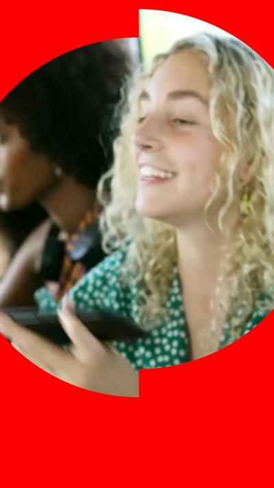A young woman with curly blonde hair listens to music on her phone on public transport.