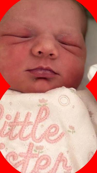 A baby girl with her eyes closed. She is wearing a a pink top with flowers on it and the words "Little Sister"