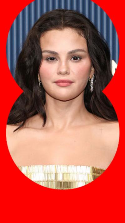 Selena Gomez looking directly forward into the camera - she has shoulder length brown hair and a gold top 