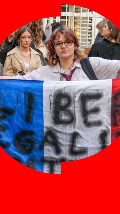 A high school student is holding a blue, white, and red tricolor flag bearing the inscription Liberte, Egalite, Fraternite in front of her high school.