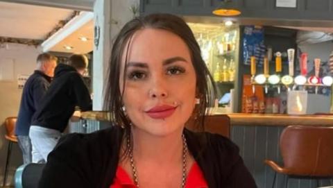 In this photo, Alice smiles at the camera and is sat in a bar