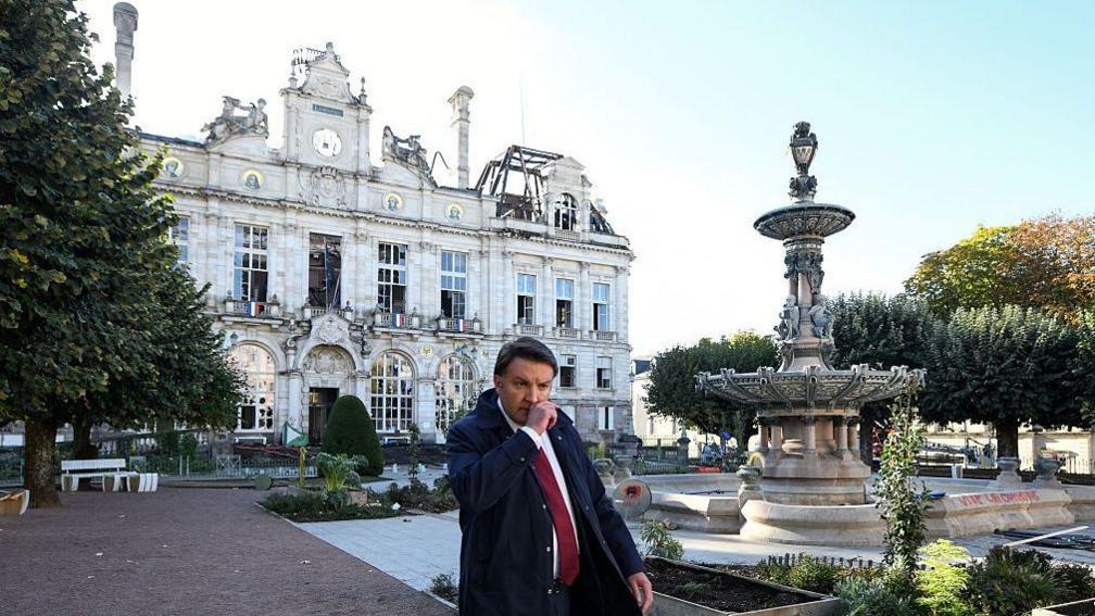 Limoges' mayor  Guillaume Guérin walks in front of the partially burnt city hall a day after riot and looting following nationwide protests against the "high cost of living"