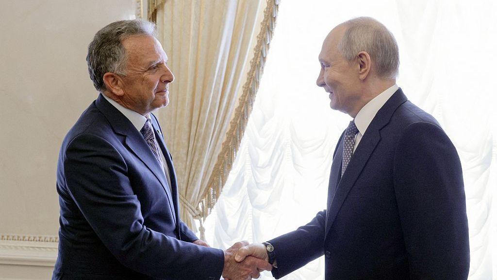 Russia's President Vladimir Putin shakes hands with US special envoy Steve Witkoff (L). Both men are wearing blue suits and smiling.