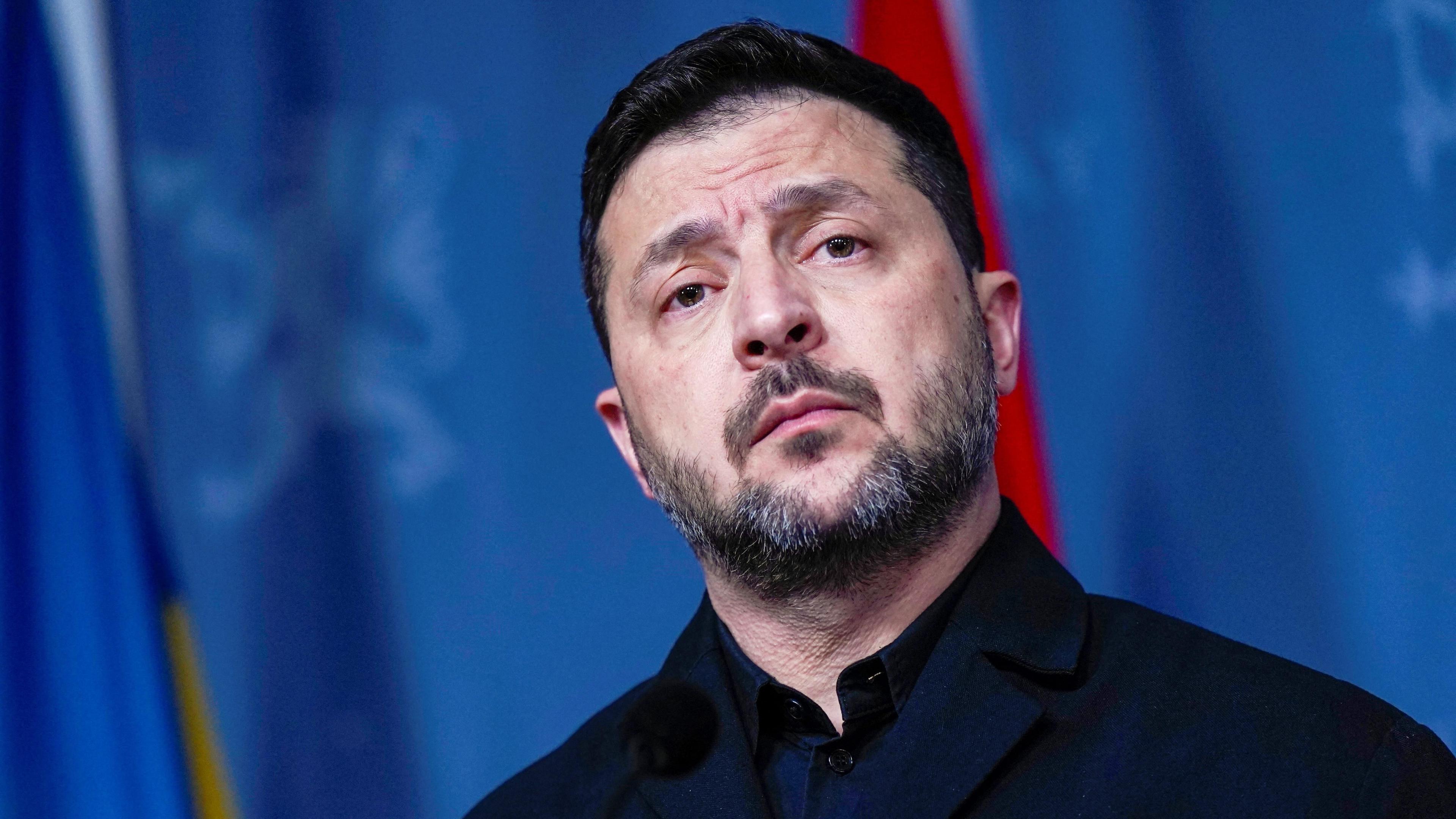 Zelensky speaking in front of a blue background wearing a high-necked black top.