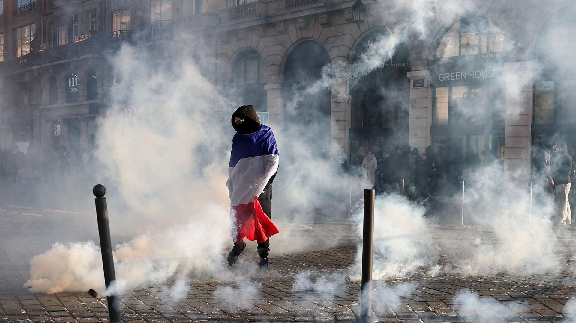 A protester wrapped in a French flag stands with smoke all around on a street in Lille on 17 October.
