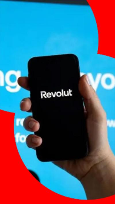 Somebody holding up a smart-phone in their right hand. The screen is black with 'Revolut' written in white letters. 