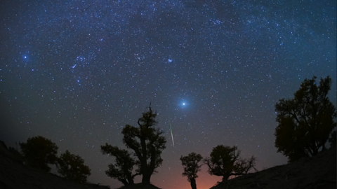 A meteor strikes across a dark blue star-filled night sky