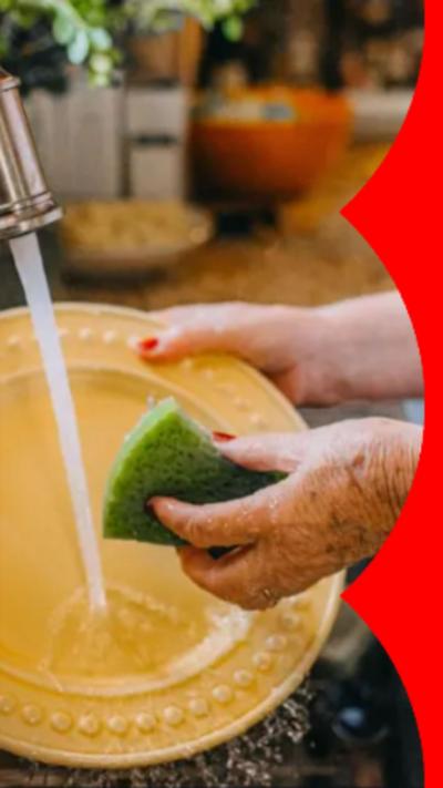 Woman washes a yellow plate with a green sponge in sink as water from the tap falls.