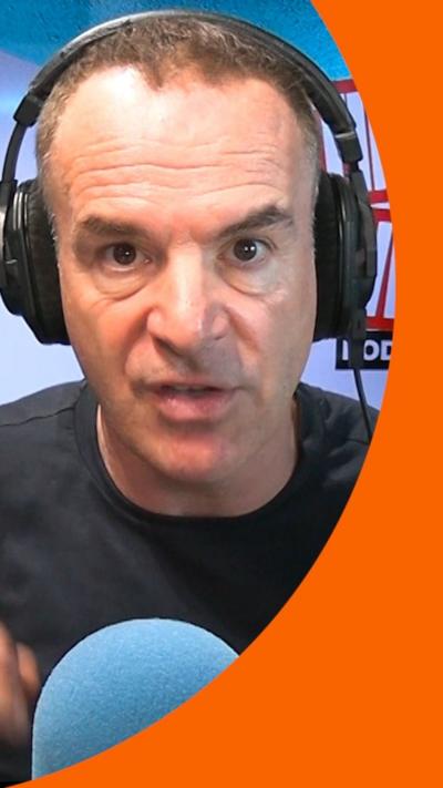 A man with short dark hair wearing headphones talks into a microphone 