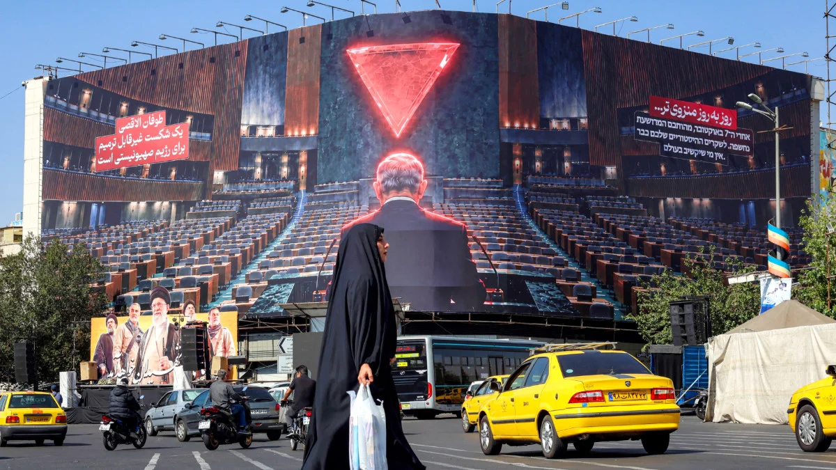 A woman walks through traffic while crossing Enghelab Square in central Tehran as a large anti-Israeli billboard is displayed behind her, on 12 October 2026 (AFP)