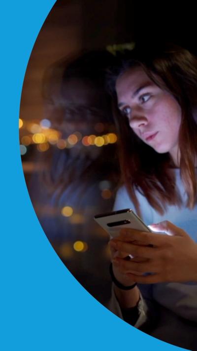 Woman stares outside window into the evening as she holds her phone