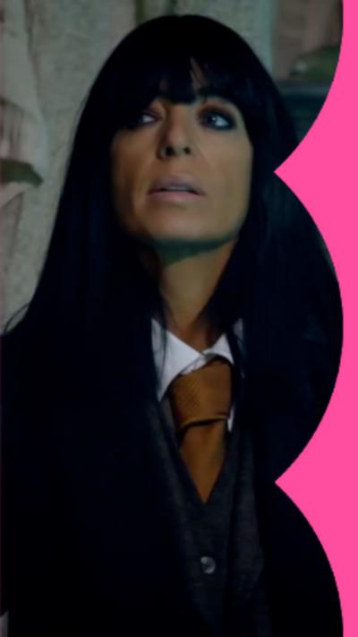 A close-up of presenter Claudia Winkleman wearing dark suit and brown tie in the dark