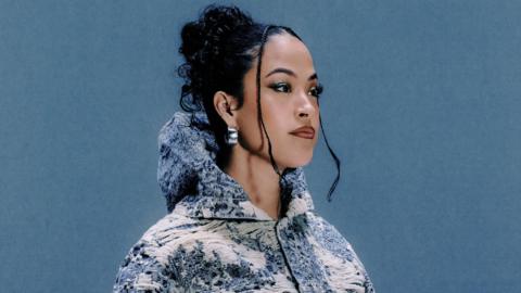 Jazzy, pictured wearing a blue and white jacket embroidered with country scenes. The 30-year-old has her dark hair tied back in a messy bun and looks to the right of the camera while posing against a denim blue backdrop.