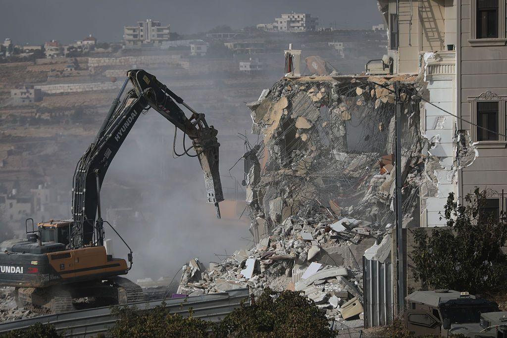 Bulldozers destroys building, creating plume of dust. 