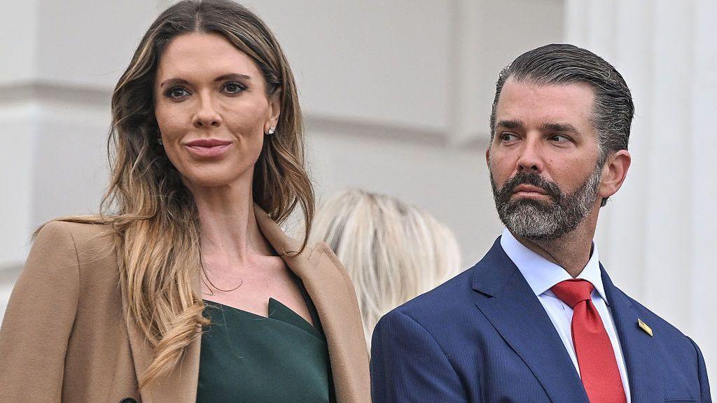  Donald Trump Jr, right, wears a blue suit and red tie as he looks at his wife Bettina Anderson Trump, who is wearing a dark green dress and dark coat, as they arrive for ceremonies in a designated viewing area inside Aras an Uachtarain on 12 September 2026, in Dublin, Ireland. 

