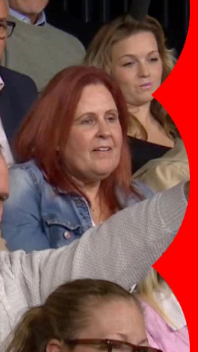 A woman with red hair, wearing a blue denim jacket, sitting in a crowd of people.