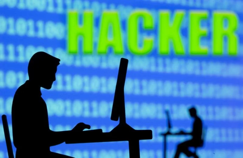A 3D printed model of men working on computers are seen in front of displayed binary code and words "Hacker\